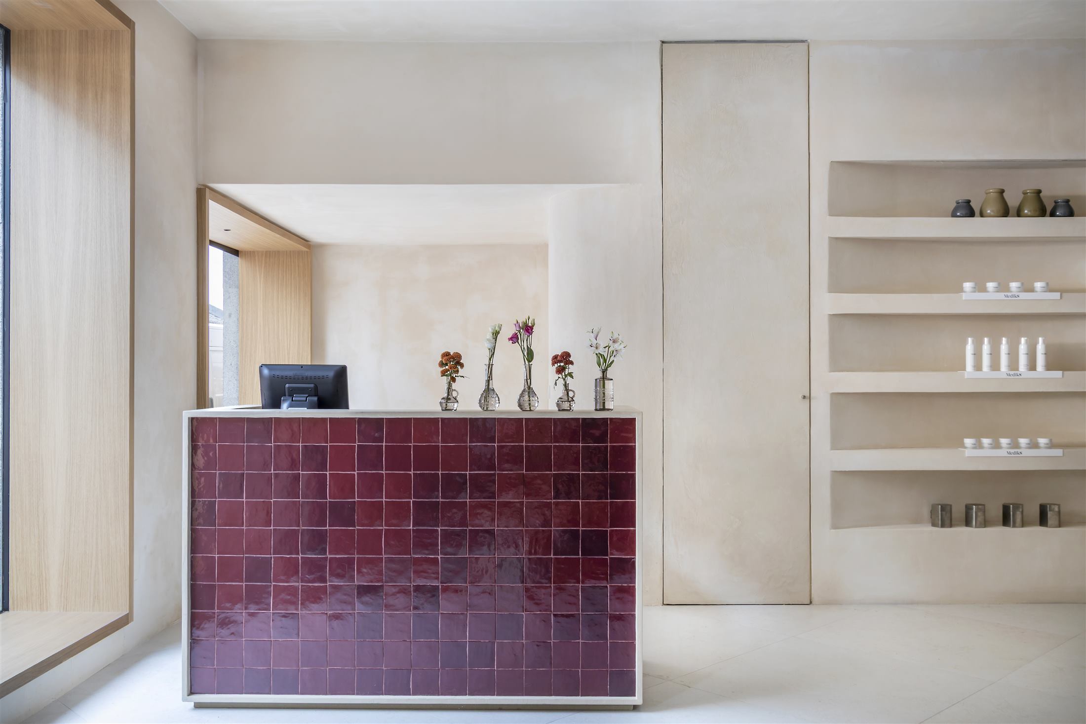 Recepción de Dotti con mostrador de azulejo granate, flores y estanterías de yeso
